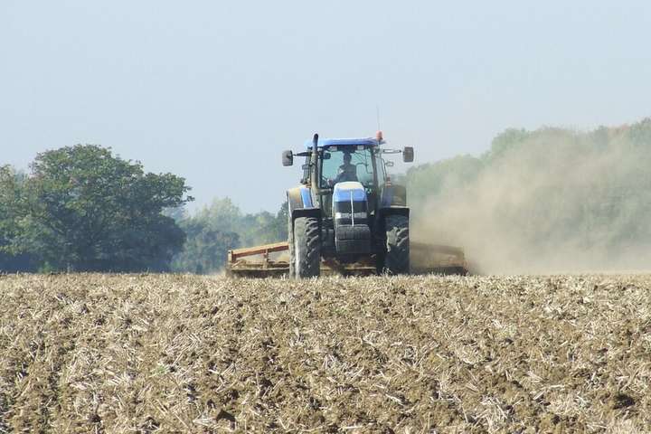 A tractor working a dry field, dust billowing behind it
